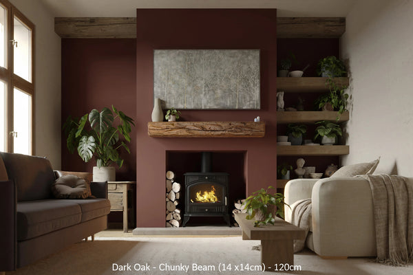 A dark oak fireplace beam installed on a red wall, supporting a mantel, with a cozy living room setting including a lit fireplace, couch, and armchair.