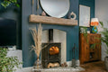 A rustic reclaimed white oak fireplace beam mounted on a blue wall above a fireplace, with decorative plants and furniture around.